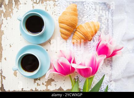 Belle tasse de café, croissants et tulipes roses sur la vieille table blanche Banque D'Images