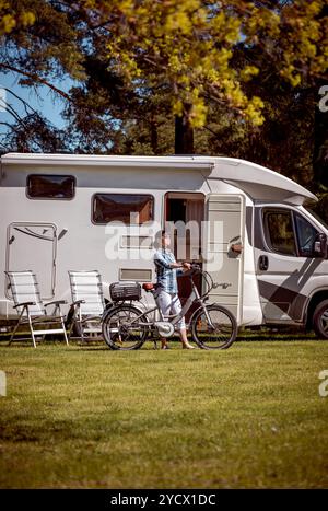 Femme sur vélo électrique reposant sur le camping. Vacances famille vacances, voyages voyage en camping-car, caravane location de vacances. Banque D'Images