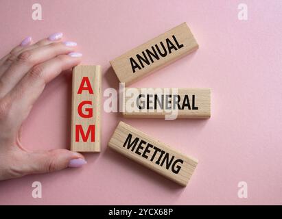 AGA - symbole de l'Assemblée générale annuelle. Mot concept AGM sur des blocs de bois. Main d'homme d'affaires. Beau fond rose. Business et AGM concept. Copier sp Banque D'Images