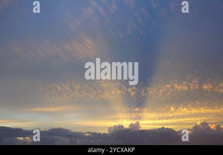 Les rayons dorés du soleil de derrière les nuages s'étendent à travers le ciel au-dessus Banque D'Images