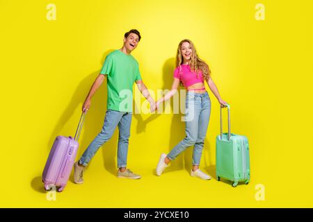 Portrait complet du corps de deux beaux jeunes partenaires tiennent la valise des bras isolé sur fond de couleur jaune vif Banque D'Images