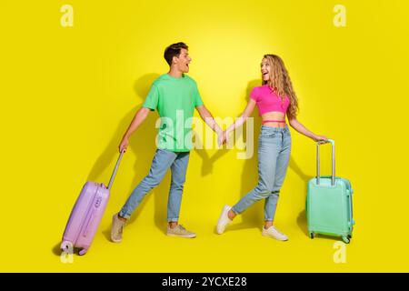 Portrait complet du corps de deux beaux jeunes partenaires tiennent la valise des bras isolé sur fond de couleur jaune vif Banque D'Images