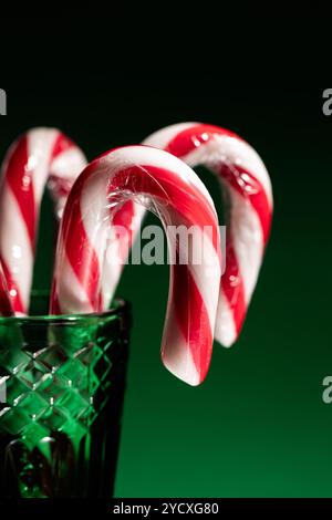 Cannes de bonbons vibrantes avec des rayures rouges et blanches, émergeant d'un vase en verre vert texturé sur un fond vert foncé, apportant une touche festive avec Banque D'Images