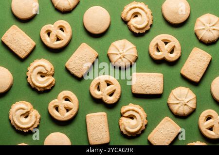 D'en haut, différentes formes de biscuits au beurre artistiquement disposés sur un fond vert vibrant, capturant l'essence festive de Noël. Banque D'Images