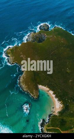 Superbe capture par drone d'une côte accidentée en Galice, avec des eaux émeraude, une crique de sable blanc et des falaises rocheuses entourées d'une végétation luxuriante Banque D'Images