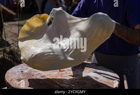 Un homme étire habilement et prépare le pain au fromage géorgien traditionnel, connu sous le nom de khachapuri, dans un cadre extérieur avec lumière naturelle du soleil highlighti Banque D'Images