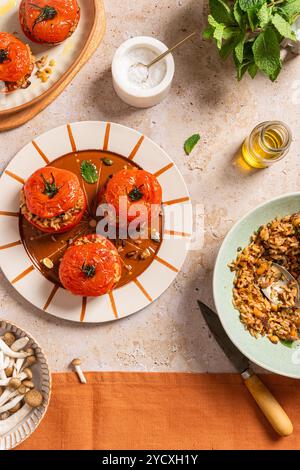 Vue de dessus d'un délicieux repas d'automne avec des tomates farcies rôties fourrées de riz brun, de noix et d'herbes, étalées artistiquement sur un plat en céramique Banque D'Images