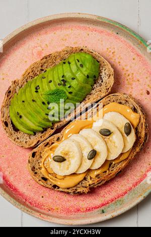 Présentoir de petit déjeuner avec deux tranches de pain grillé de grains entiers, l'une garnie de tranches d'avocat et de graines de sésame noir, et l'autre avec du beurre d'arachide, b. Banque D'Images