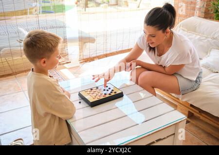 Une mère et son jeune fils aiment se lier autour d'un jeu de société dans une pièce ensoleillée confortable, démontrant un joyeux moment en famille Banque D'Images