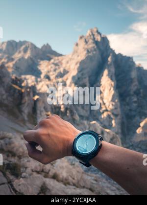 Vue rapprochée de la main d'un randonneur anonyme portant une smartwatch affichant une carte, sur fond accidenté des sommets des Picos de Europa Banque D'Images