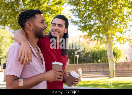 Un couple gay profite d'une journée sereine dans un parc urbain, ils partagent des sourires chaleureux et une conversation décontractée autour d'un café, illustrant l'amour et le bonheur dans un mul Banque D'Images