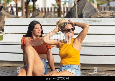 Une mère et sa fille transgenre se détendent et se lient par une journée ensoleillée, assis sur des marches blanches, partageant des rires et engageant des conversations tout en regardant Banque D'Images