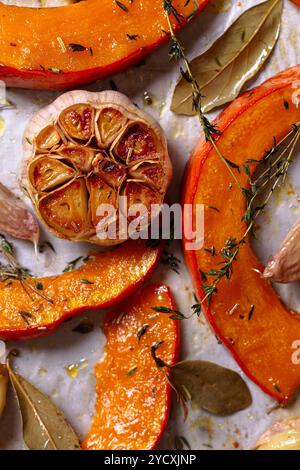 Vue de dessus de tranches de citrouille fraîches cuites au four avec de l'ail rôti et des herbes aromatiques, y compris la feuille de laurier et le thym sur une plaque de cuisson. Parfait pour automne-inspir Banque D'Images