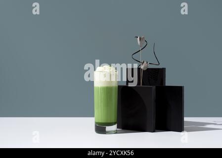 Un grand verre de thé matcha frais recouvert de crème fouettée, présenté dans un décor minimaliste élégant avec un subtil accent floral. Banque D'Images
