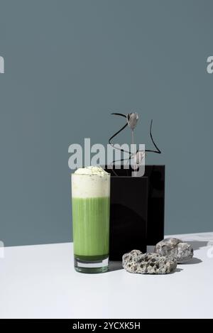 Un grand verre rempli de thé matcha vert éclatant recouvert de crème fouettée moelleuse, présenté dans un décor minimaliste avec un élégant arra floral Banque D'Images