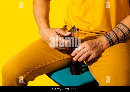 Une image vibrante mettant en scène un homme portant une tenue jaune alors qu'il ouvre habilement une bouteille en verre foncé avec un ouvreur en métal le fond jaune vif en Banque D'Images