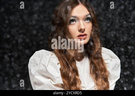 Une charmante jeune femme aux cheveux longs lève les yeux avec soin tandis qu'une toile de fond chatoyante l'entoure. Banque D'Images