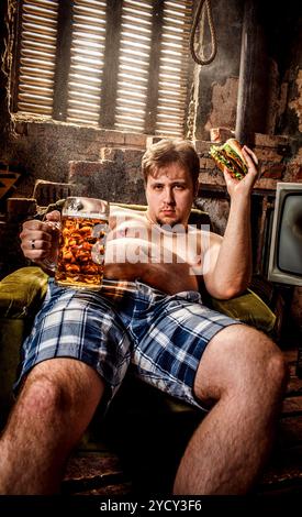 Fat Man eating a hamburger assis sur une chaise dans les bidonvilles Banque D'Images