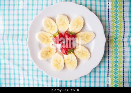 Banane et fraises sur une assiette blanche et une serviette colorée Banque D'Images