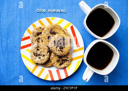 Oatmeal Cookies au chocolat sur fond bleu serviette et deux tasses de café, bonjour l'inscription Banque D'Images