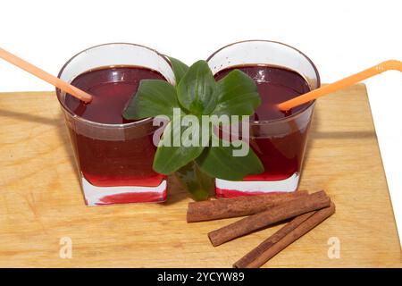 Sirop de groseille rouge dans des verres sur une planche de bois sur fond blanc et bâtonnets de cannelle. Banque D'Images