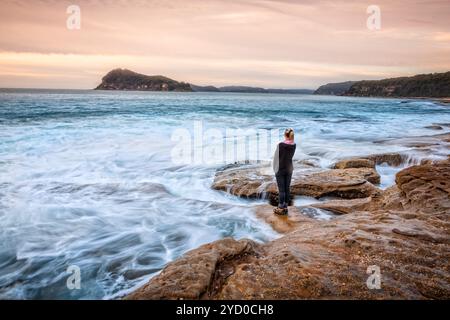 Femelle debout sur des rochers laissant les vagues côtières se laver jusqu'à ses pieds Banque D'Images