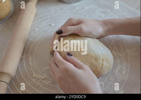 Ingrédients de cuisson pour la cuisson des petits pains sucrés, les mains de la femme pétrissent la pâte sur un tapis de silicone Banque D'Images