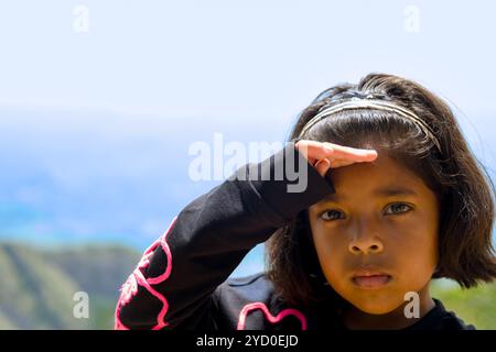 Jeune fille protégeant ses yeux du soleil brillant avec un regard déterminé sur son visage. Banque D'Images