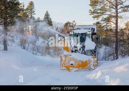 Tracteur chasse-neige avec souffleuse montée à l'arrière nettoyant une route de montagne enneigée, poussant la neige en l'air. Paysage hivernal, entretien des routes, sno Banque D'Images