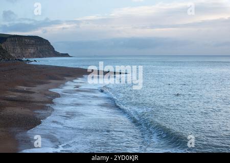 Rivage tranquille à la plage de Rock-a-Nore, Hastings, avec des vagues calmes et des nageurs de mer lointains en hiver sous un ciel couvert. Banque D'Images