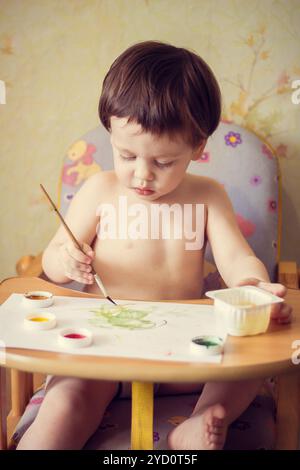 Le garçon peint sur papier. Peinture rouge et jaune. Les activités des enfants. Passe-temps de l'enfant. Dimensions Banque D'Images