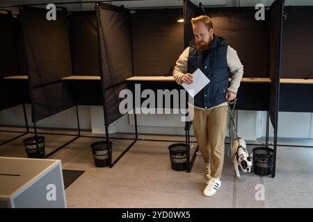 Vilnius, Lituanie. 24 octobre 2024. Un homme avec chien quitte le bureau de vote d'un bureau de vote pendant le vote anticipé pour le deuxième tour des élections législatives. Le deuxième tour des élections législatives en Lituanie aura lieu le 27 octobre. Le Parti social-démocrate de l'opposition a pris la première place au premier tour, mais son avance sur les conservateurs au pouvoir est minime. Crédit : SOPA images Limited/Alamy Live News Banque D'Images