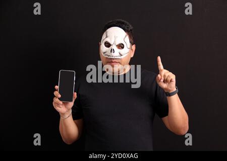 Homme adulte mexicain avec masque de crâne utilise son téléphone portable pour profiter des promotions et réductions du jour des morts au Mexique Banque D'Images