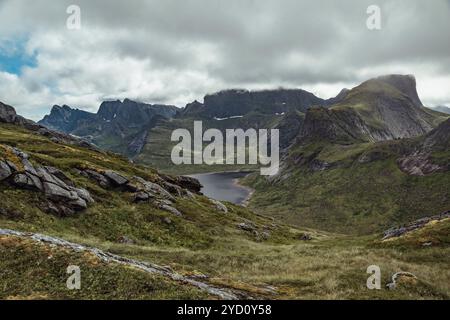 Un vaste paysage se déploie avec des collines ondoyantes et des pics montagneux spectaculaires dans les îles Lofoten, dans le Nordland. Des nuages épais planent au-dessus de lacs sereins et de lus Banque D'Images