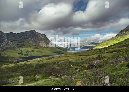 Explorez les paysages époustouflants des îles Lofoten, où les collines verdoyantes rencontrent des lacs tranquilles sous un ciel étonnant rempli de nuages, accueillant en plein air Banque D'Images