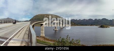 Le pont Gimsoystraumen enjambe gracieusement les eaux tranquilles d'un réservoir dans les îles Lofoten, entouré de montagnes et de verdure luxuriante. Banque D'Images