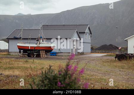 Dans les îles Lofoten, un bateau repose sur une remorque près d’une charmante maison, entourée de prairies et de montagnes sous un ciel nocturne. Le cadre serein Banque D'Images