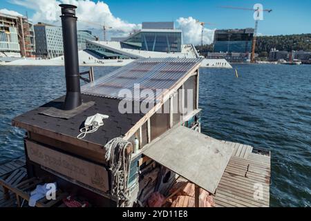 Un bâtiment en bois se trouve sur le quai d'Oslo, offrant une vue tranquille sur l'opéra moderne et le front de mer animé, entouré de grues et d'un Banque D'Images