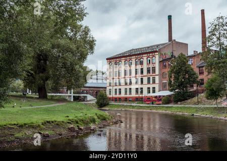 Un charmant bâtiment à usage mixte se dresse à côté d'un canal tranquille à Oslo, entouré d'herbe luxuriante et d'arbres, avec des reflets chatoyants dans l'eau Banque D'Images