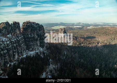 Une vue imprenable capture les falaises spectaculaires des Badlands en Saxe suisse, entourées d'une forêt dense recouverte de neige sous un soleil éclatant Banque D'Images