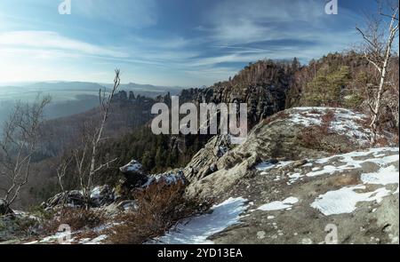 Un panorama à couper le souffle montre un paysage hivernal avec des collines enneigées et des escarpements rocheux en Saxe suisse, sous un ciel ensoleillé. Banque D'Images