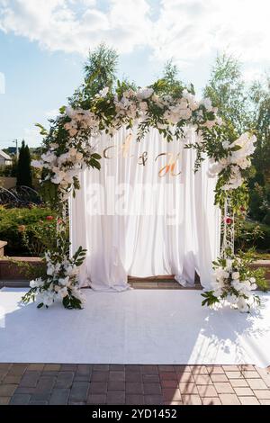 Élégante arche de mariage florale avec draperie blanche et initiales dorées. Banque D'Images