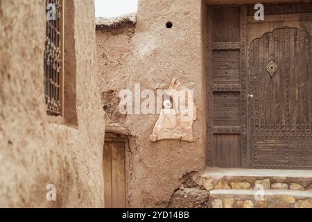 Ce site historique présente un relief en pierre magnifiquement sculpté et une porte traditionnelle en bois, serrée contre un mur beige altéré dans la terre aride du Maroc Banque D'Images