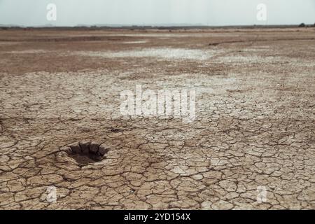 La surface desséchée d'un lit de lac sec révèle de la terre fissurée et une petite dépression, mettant en évidence les effets de la sécheresse dans le désert du Sahara, au Maroc, Banque D'Images