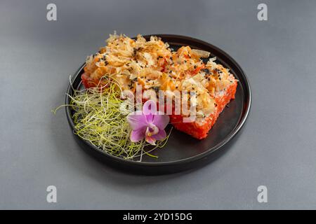 Délicieux rouleaux de sushi servis sur une assiette noire avec des microgreens et une fleur d'orchidée sur un fond gris Banque D'Images