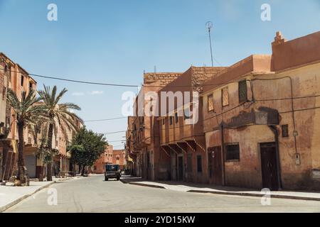 Une rue calme et ensoleillée dans un quartier marocain présente des bâtiments beiges, des palmiers et un style architectural classique. Les véhicules passent sur un d chaud Banque D'Images