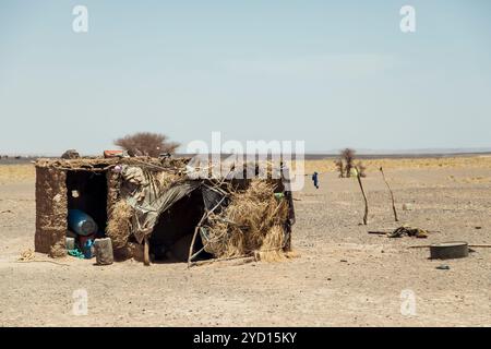 Dans le vaste désert du Sahara du Maroc, une simple cabane faite de matériaux naturels résiste au paysage sec. L'horizon s'étend sans fin Banque D'Images