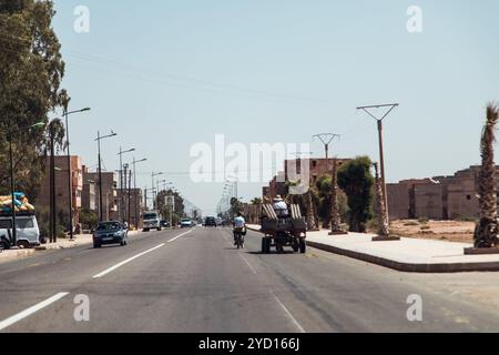 Dans le centre-ville du Maroc, une rue urbaine animée présente divers véhicules et piétons naviguant sur la route sous un ciel dégagé. De grands palmiers bordent le Banque D'Images