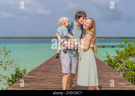 Maman, papa et leur bébé fils explorant la jetée en bois au-dessus des eaux turquoises du lac Bacalar, au Mexique. Concept de destination de voyage tropical paisible Banque D'Images