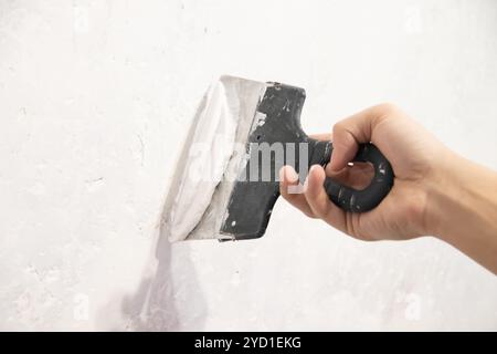 Main masculine avec un mur de mastic de spatule. . Alignez le mur. Mur blanc. Mastic sur le mur Banque D'Images